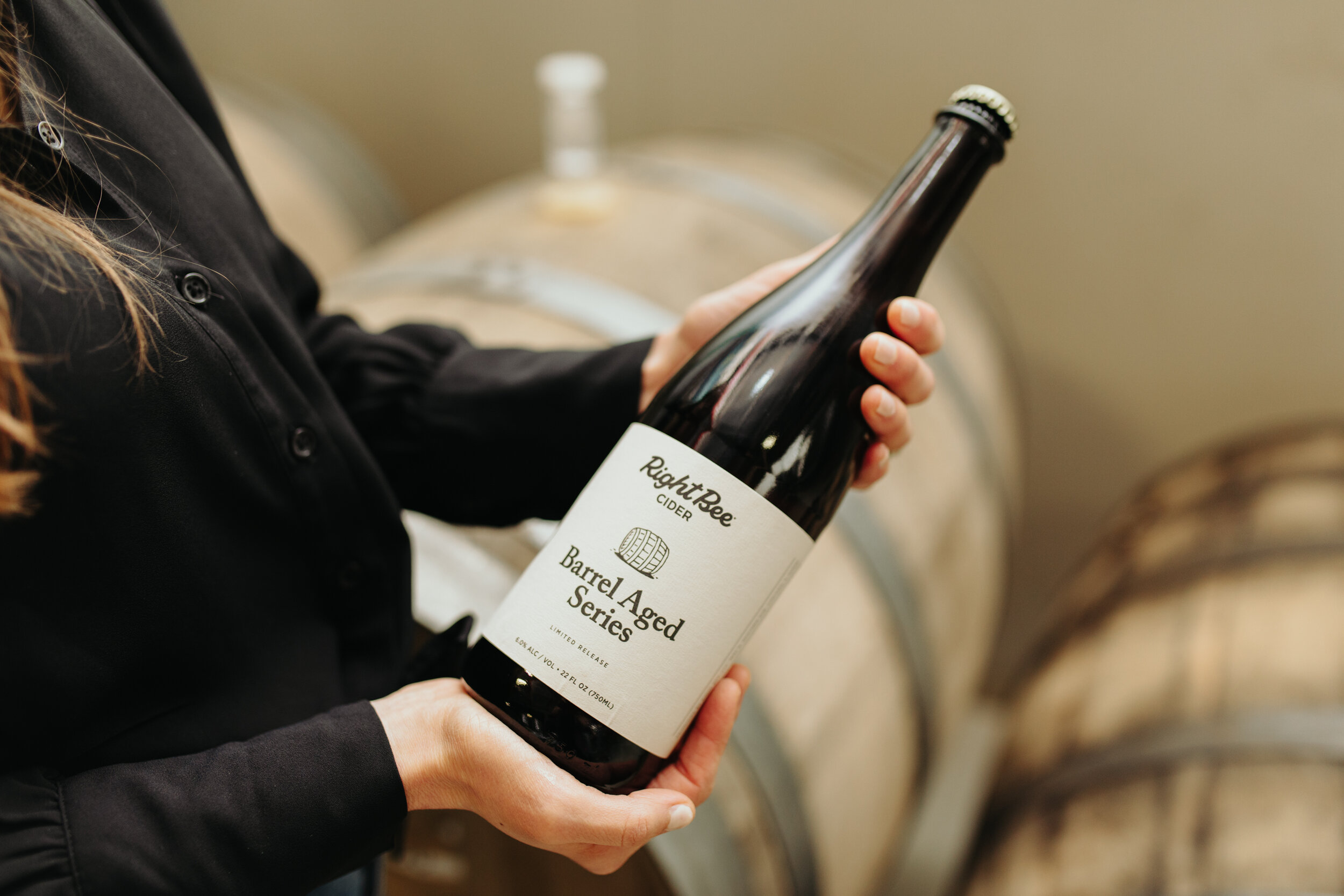 Cidermaker holding a bottle in front of barrels